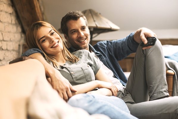 AdobeStock_288763235_Paar-mit-Fernbediehnung-auf-Couch