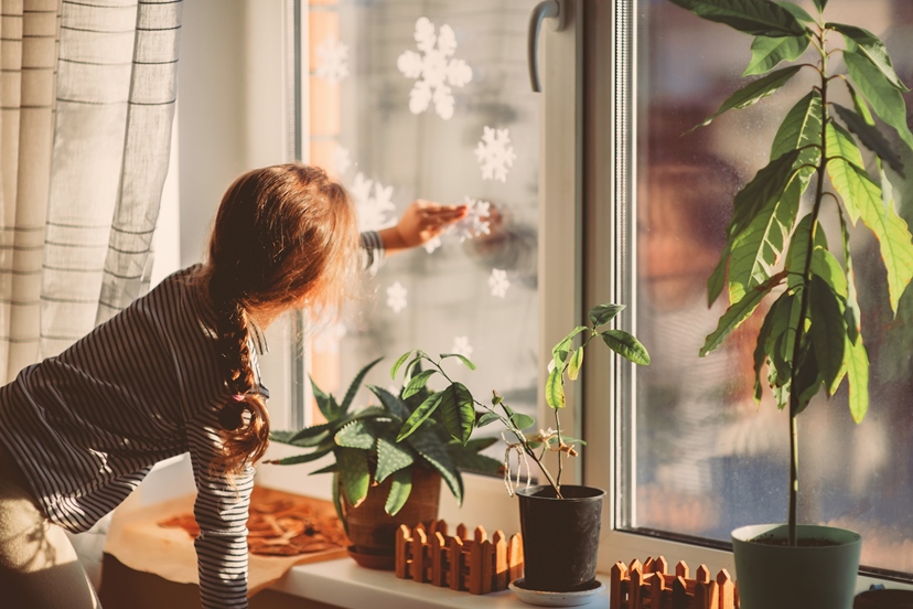 AdobeStock_468423563_Maedchen klept Schneeflocke auf Fenster