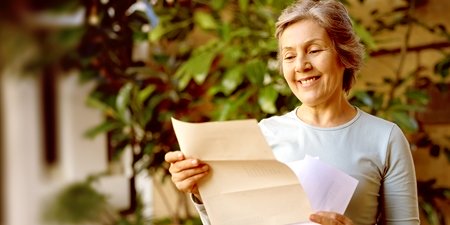 Glückliche ältere Frau zu Hause, die einen Brief liest, den sie in der Post bekommen hat und lächelt.